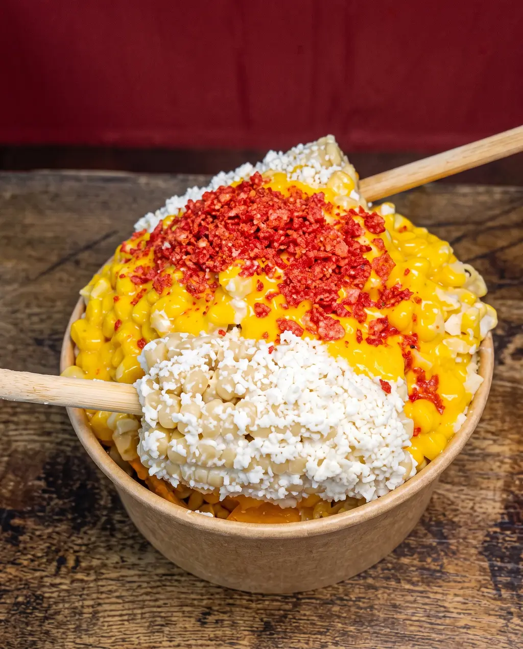 Un vaso de esquites de Poloco: elote amarillo cubierto de queso cotija y chile rojo